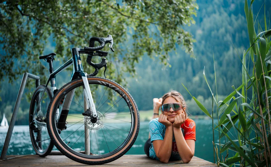 Bike Boutique Hotel Lindenhof **** © Martin Hofmann Frau liegt auf Holzsteg neben Fahrrad am See mit Bergen im Hintergrund