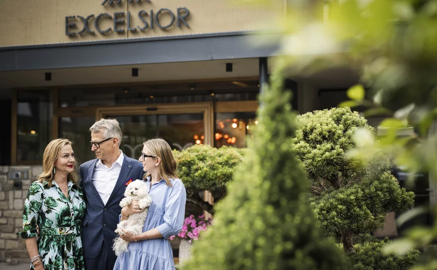 Excelsior Dolomites Life Resort ****S © Hannes Niederkofler Drei Personen und ein Hund vor dem Hotel Excelsior