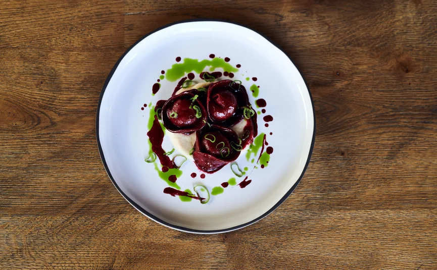 Three red tortellini with green sauce and garnish on white plate