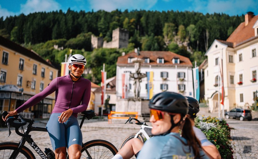 Cyclists in sportswear resting in a town square with a castle in the background