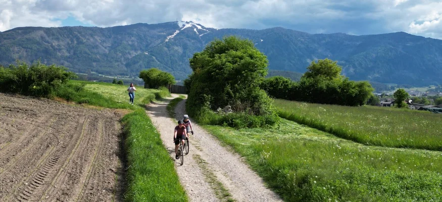 Cyclists on dirt path with mountains and cloudy sky in background