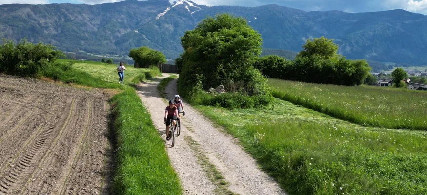 Neue Gravelbike Holidays Hotels 2026 © Hotel Innerhofer - Gisse Zwölf Radfahrer auf Feldweg mit Bergen im Hintergrund bei bewölktem Himmel
