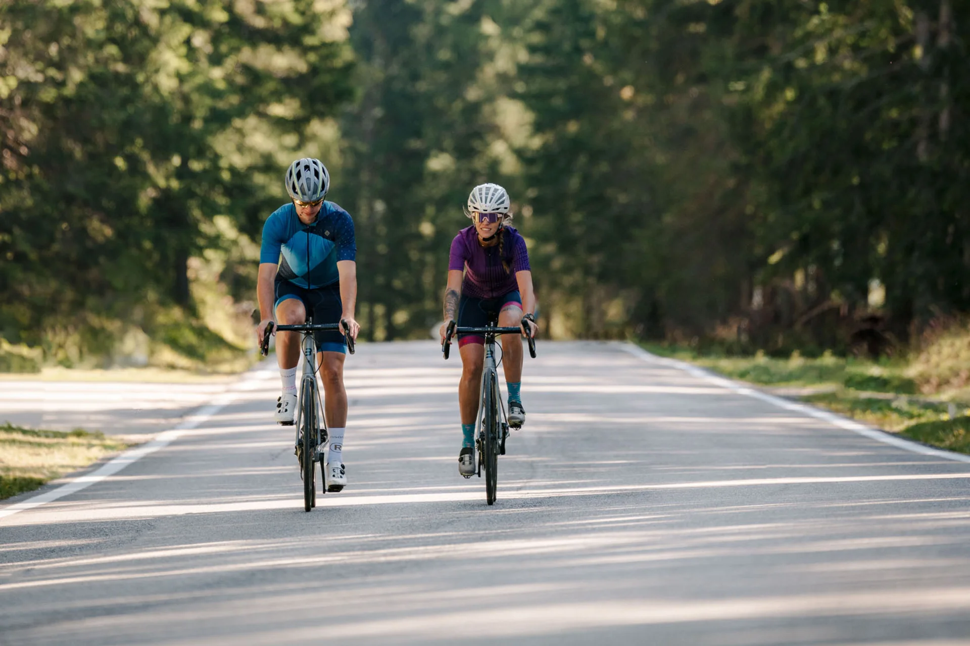 Zwei Radfahrer auf einer Straße im Wald mit Berg im Hintergrund