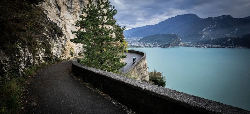 Northern Lake Garda © Gijs Ferkranus - Wielrenblad Magazine Cyclist on winding mountain road above a large lake with cloudy sky