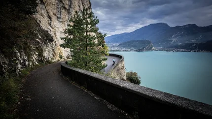 Cyclist on winding mountain road above a large lake with cloudy sky