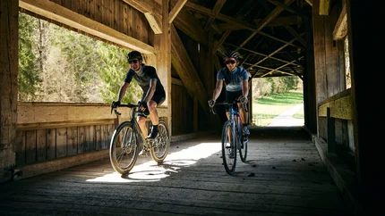 Two cyclists riding through a wooden covered bridge in daylight