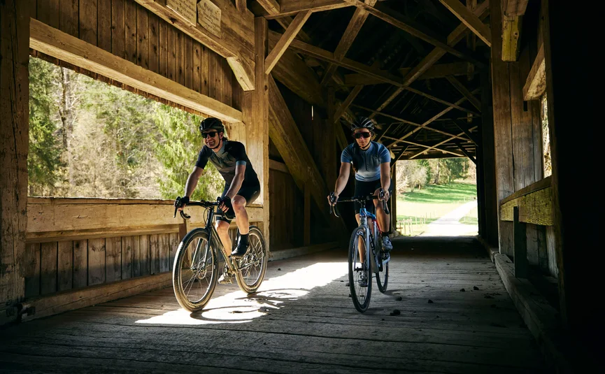 Two cyclists riding through a wooden covered bridge in daylight