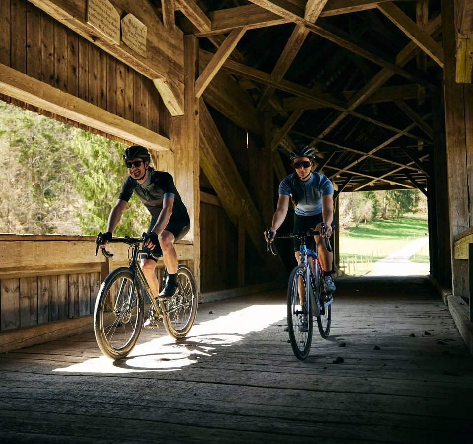 Zwei Radfahrer fahren durch eine hölzerne gedeckte Brücke bei Tageslicht
