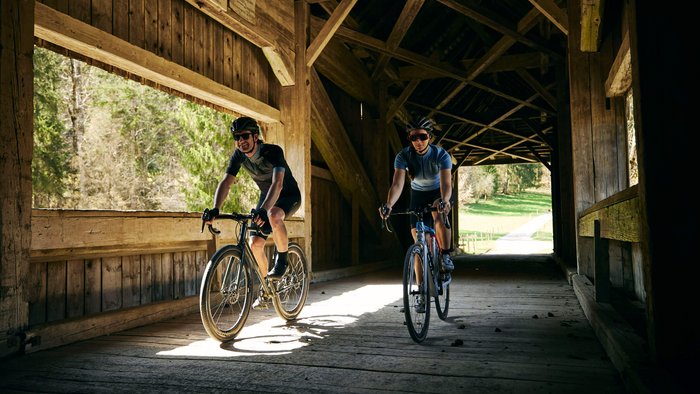 Zwei Radfahrer fahren durch eine hölzerne gedeckte Brücke bei Tageslicht