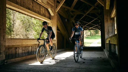 Zwei Radfahrer fahren durch eine hölzerne gedeckte Brücke bei Tageslicht
