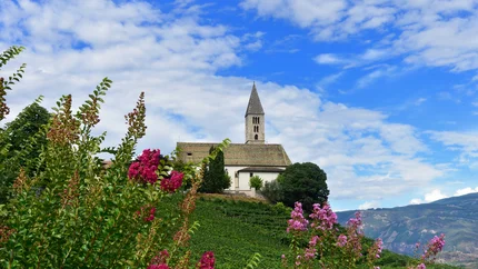 Kirche auf einem Hügel mit blühenden Sträuchern und Bergen im Hintergrund