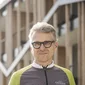 Older man holding bike helmet standing with bicycle in front of building