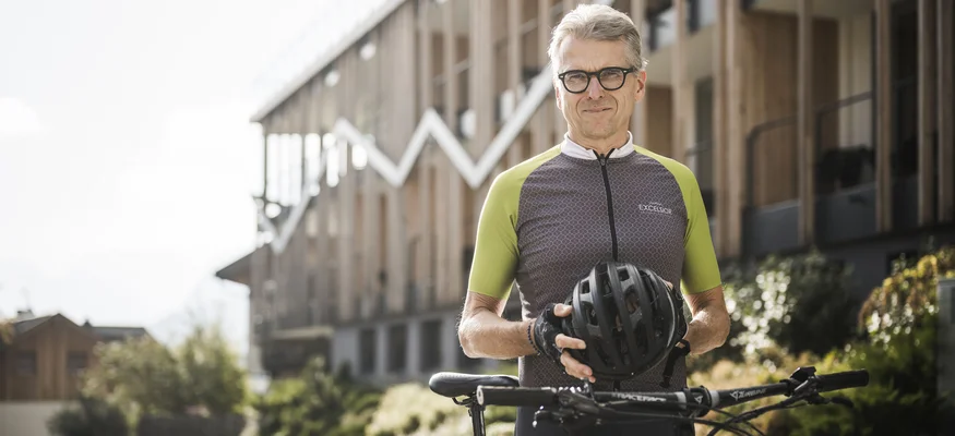 Älterer Mann mit Fahrradhelm und Rad vor modernem Gebäude
