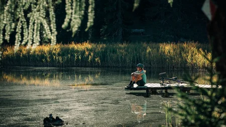 Das waren die Golden Days in Nauders © TVB-Tiroler-Oberland-Nauders-Christian-Penning - Pause am See Person sitzt neben einem Fahrrad auf einem Steg an einem von Schilf umgebenen See