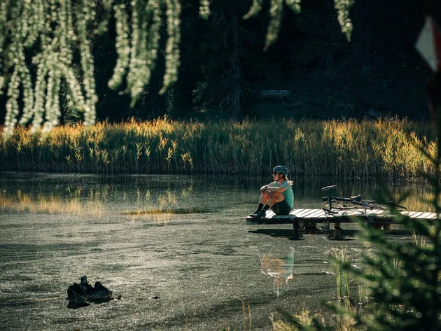 Das waren die Golden Days in Nauders © TVB-Tiroler-Oberland-Nauders-Christian-Penning - Pause am See Person sitzt neben einem Fahrrad auf einem Steg an einem von Schilf umgebenen See