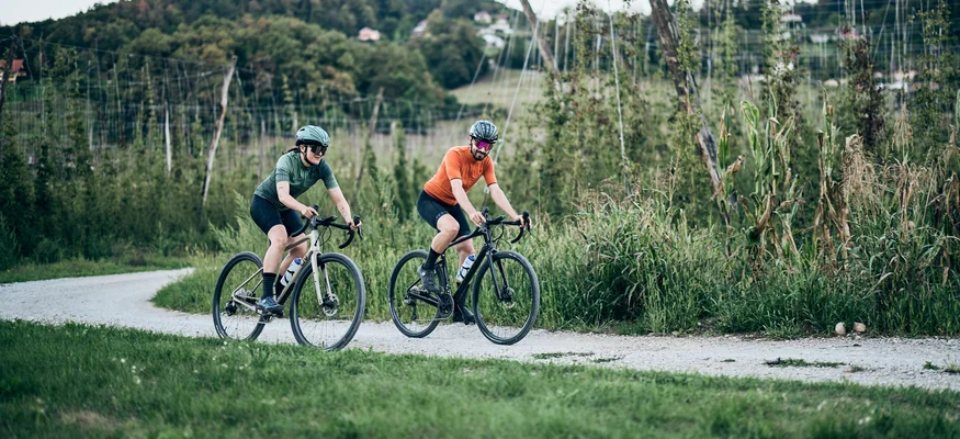 Zwei Radfahrer fahren auf einem Schotterweg durch eine grüne Landschaft