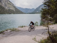 Fahrradfahrer auf Schotterweg neben See und Bergen