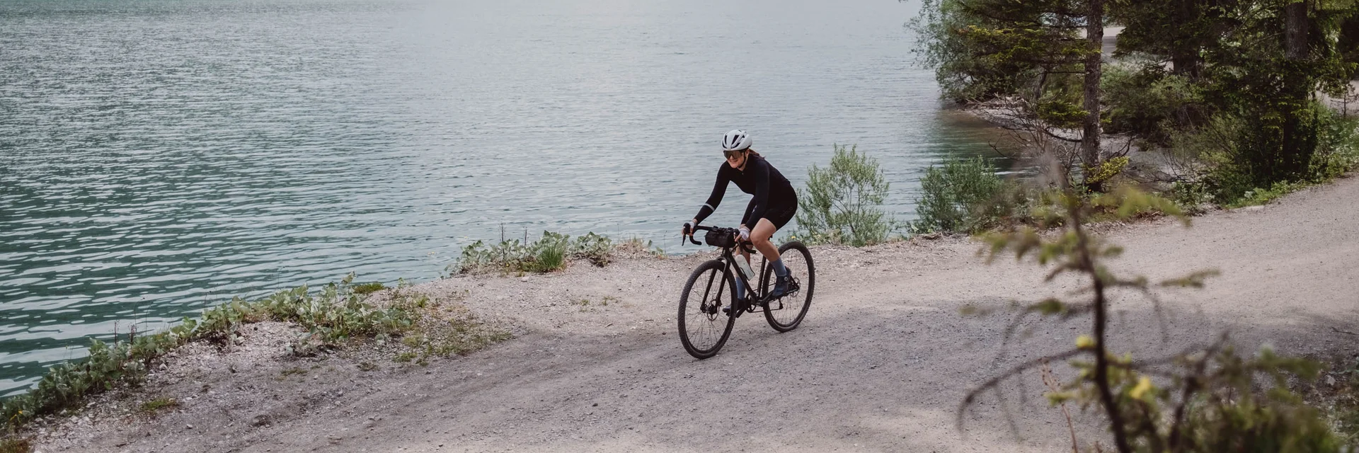 Cyclist riding on gravel path beside lake with mountains