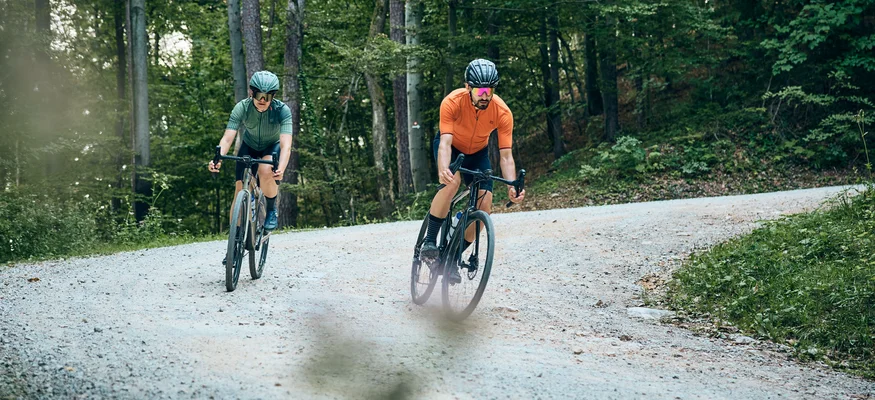 Zwei Radfahrer fahren auf einem Waldweg auf schottriger Strecke
