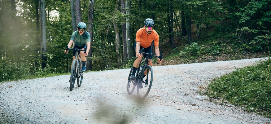 Zwei Radfahrer fahren auf einem Waldweg auf schottriger Strecke