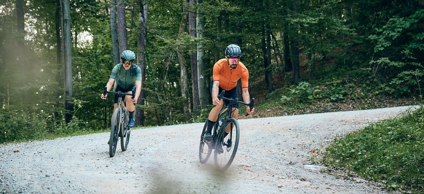 Zwei Radfahrer fahren auf einem Waldweg auf schottriger Strecke