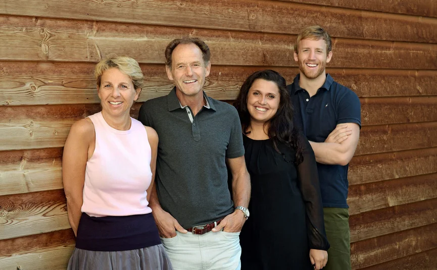 Vier lächelnde Personen stehen vor einer Holzwand