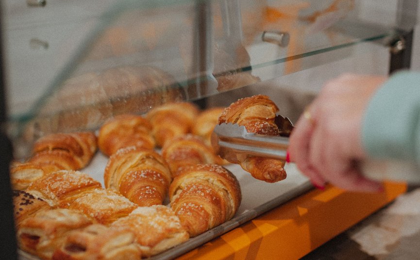 Jemand nimmt Croissant mit Zange aus einer Bäckereivitrine