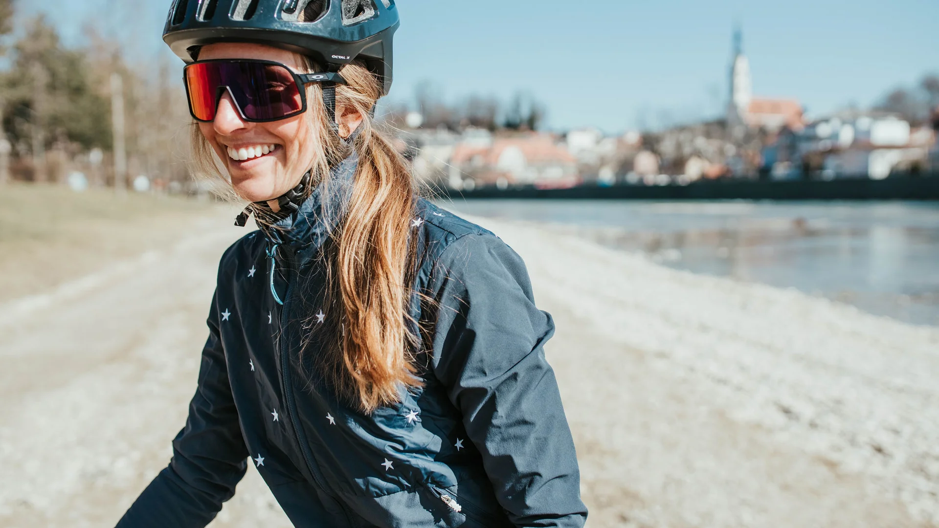 5 Tipps fürs Graveln in Oberbayern © Elisabeth Kellerer Frau mit Helm und Sonnenbrille lächelnd am Flussufer bei Sonnenschein
