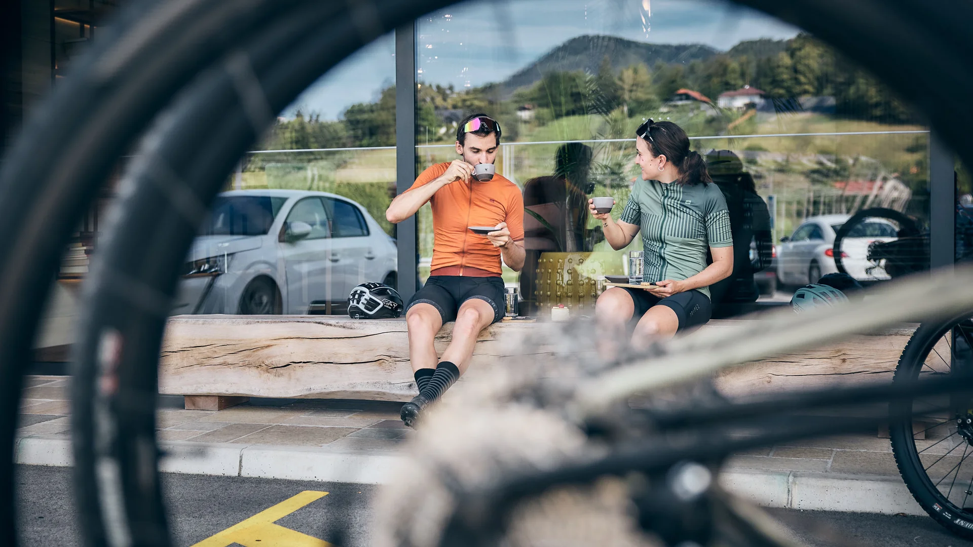 Zwei Radfahrer trinken Kaffee auf Bank, Fahrradreifen im Vordergrund