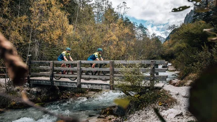Zwei Radfahrer überqueren eine Holzbrücke über einen Bach im Wald