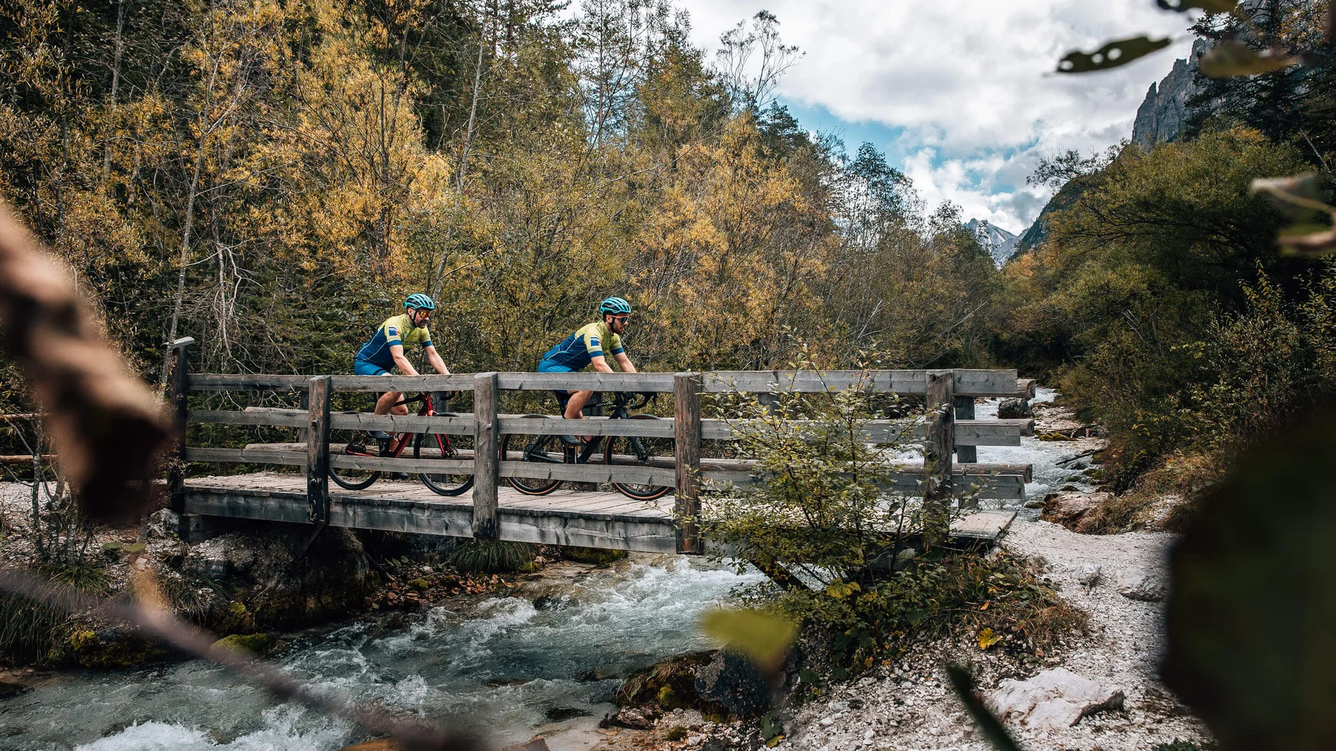 Zwei Radfahrer überqueren eine Holzbrücke über einen Bach im Wald