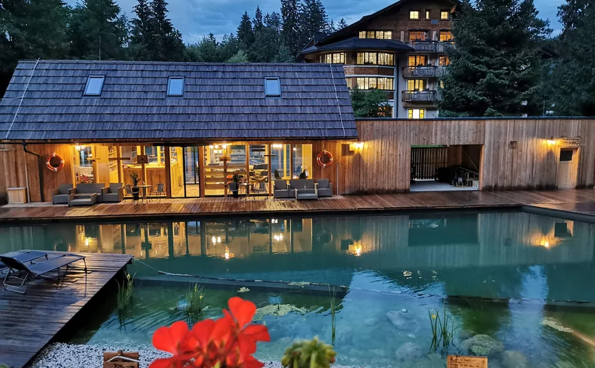 Lit wooden house with pool and flowers at dusk