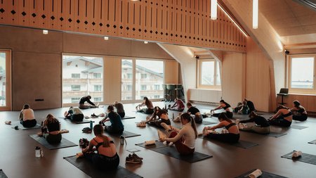 Gruppe dehnt sich auf Yogamatten in einem modernen Holzraum mit großen Fenstern