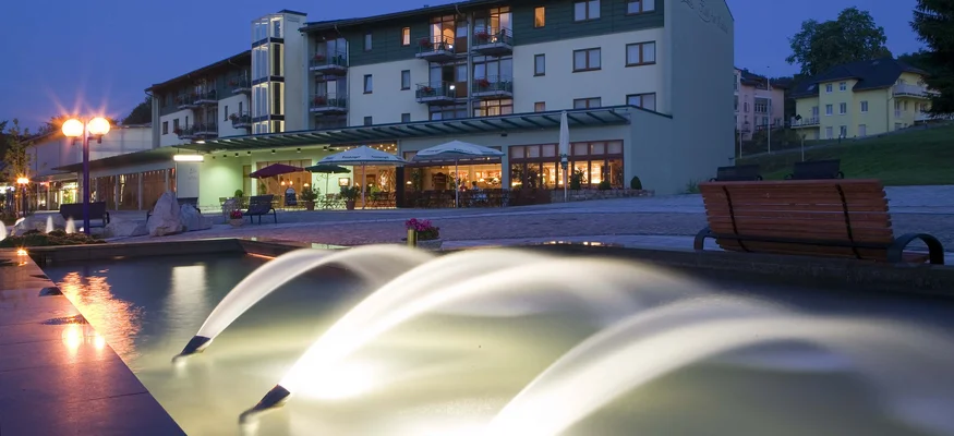 Beleuchtete Wasserspiele mit einem modernen Gebäude bei Abenddämmerung