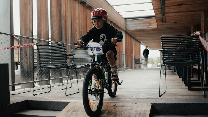 Kind mit Helm fährt Fahrrad eine Rampe in modernem Gebäude hinunter