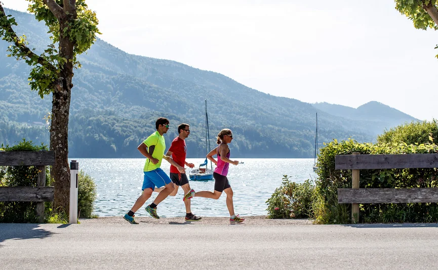 Three people jogging by a lake with mountains in the background