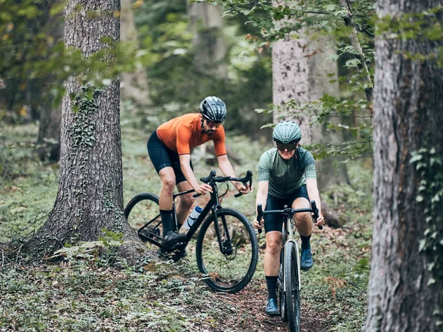 Qualitätsversprechen © Tobias Köhler Zwei Radfahrer fahren durch einen Wald auf einem schmalen Pfad