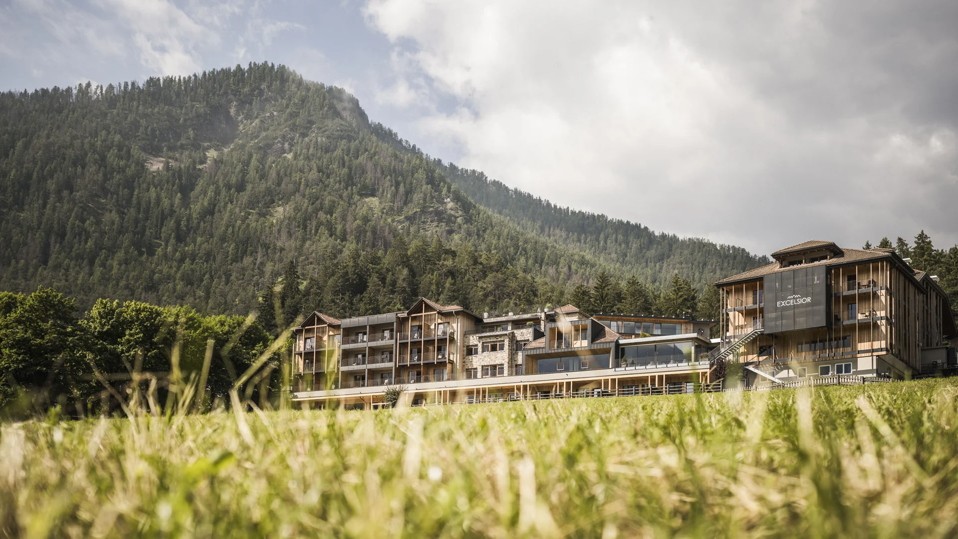 Hotel Excelsior vor bewaldetem Berg bei bewölktem Himmel