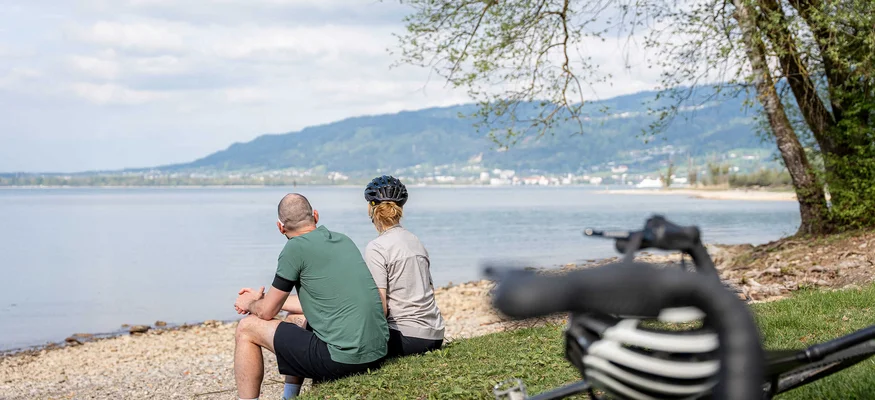 Gravelbiken in Vorarlberg: Die 7 schönsten Highlights zwischen Bodensee und Alpen © Chris Gollhofer - Vorarlberg Tourismus Zwei Radfahrer sitzen am Seeufer und genießen die Aussicht auf das Wasser und die Berge