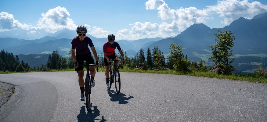 Salzburger Sportwelt © Christina Neubauer Zwei Radfahrer fahren auf Bergstraße mit Alpenkulisse bei sonnigem Wetter