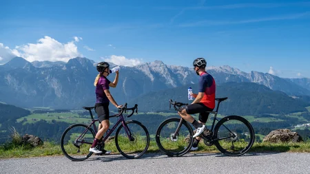 Zwei Radfahrer trinken Wasser mit Bergpanorama im Hintergrund