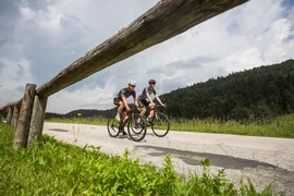 Gravel bike holiday at Lake Levico © Heiko Mandl Two cyclists on country road next to green grass and forest under cloudy sky