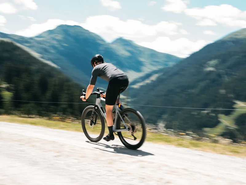 Gravelbike Holidays © Martina Wunderle / Flo Distl Fahrradfahrer auf Bergstraße mit Bergen im Hintergrund