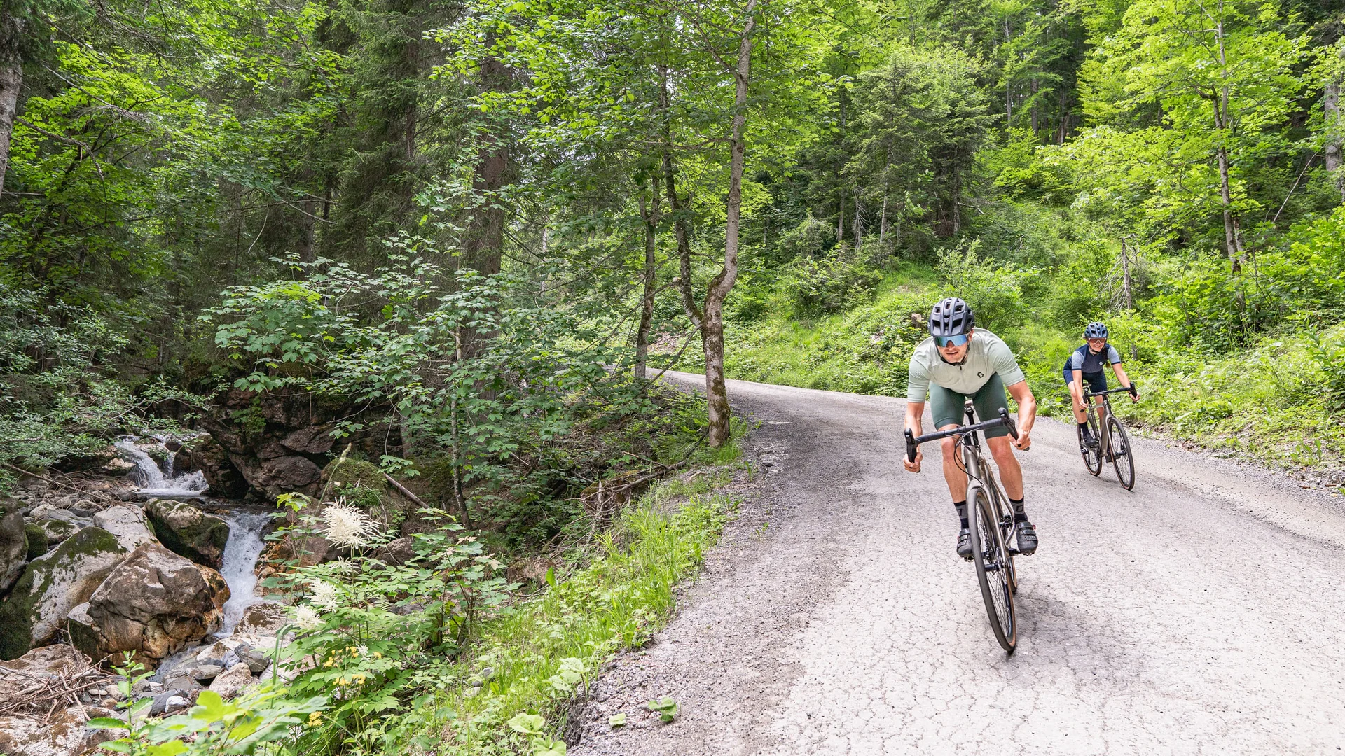 Zwei Radfahrer fahren auf einem Waldweg neben einem Bach