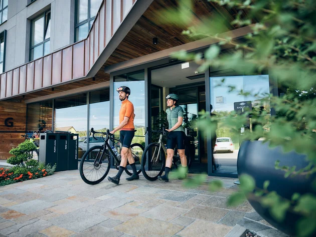 Two cyclists in sportswear walking with their bikes out of a modern building