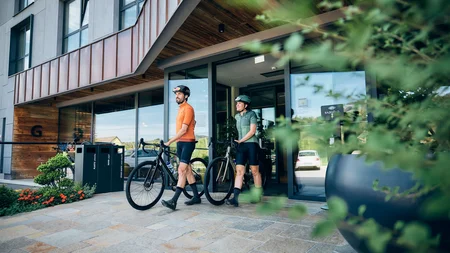 Two cyclists in sportswear walking with their bikes out of a modern building