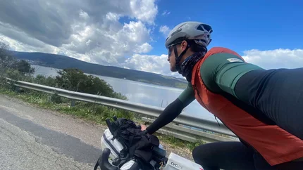 Radfahrer mit Helm und Ausrüstung fährt an einem See vorbei unter bewölktem Himmel