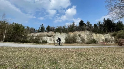 Cyclist riding on gravel path with forested hill and blue sky background