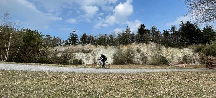 Cyclist riding on gravel path with forested hill and blue sky background