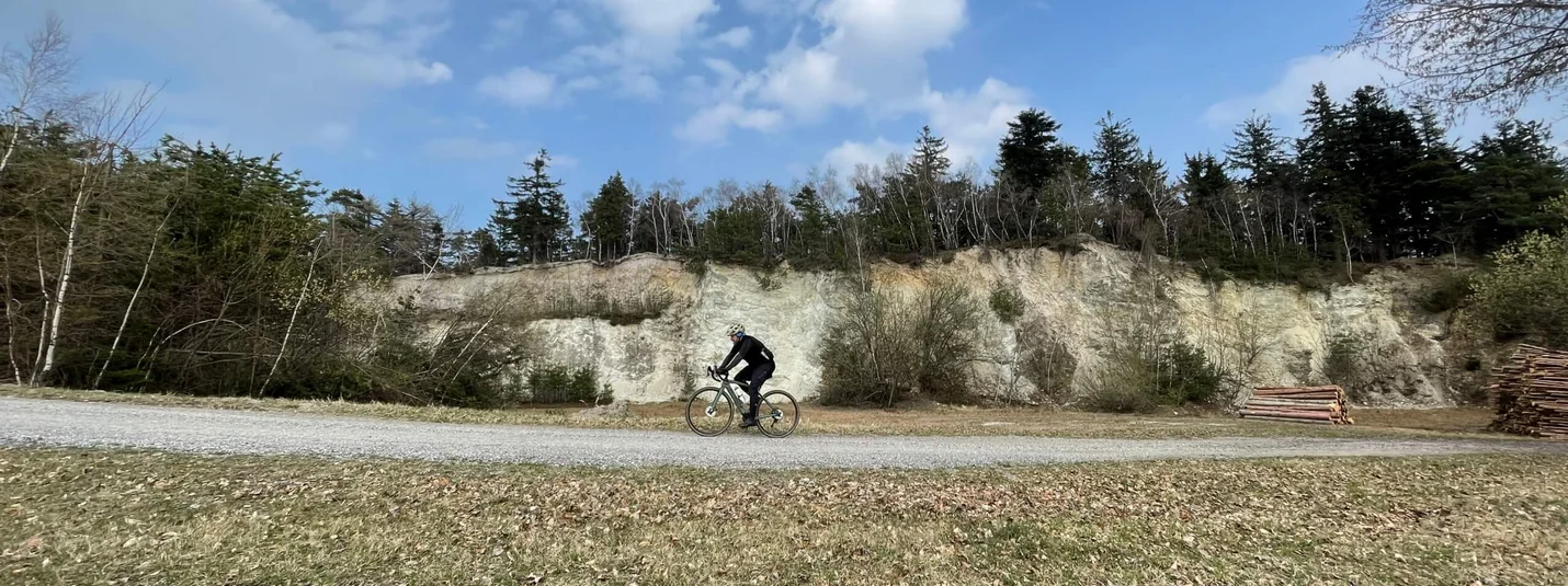 Gravel week Bucklige Welt © Landgasthof Krumbacherhof Cyclist riding on gravel path with forested hill and blue sky background